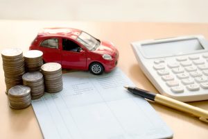 Stacked coins in columns alongside a savings book and a car, symbolizing concepts of finance, savings, and banking.