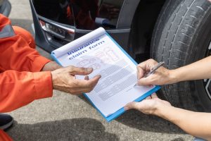 An insurance agent examines a damaged car after a road accident, assisting the car owner with paperwork as the insurance team processes the claim.