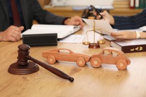 Close-up of wooden car models and a judge's gavel on a lawyer's desk during a meeting in the office, symbolizing legal discussions about car accident cases.