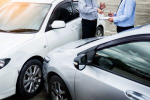 An insurance agent examines a car and writes on a clipboard while assessing and processing an accident claim.