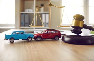 Two small car models placed on a table in a courtroom, with a gavel nearby. The scene represents a road crash case, highlighting law, justice, lawyer services, and a civil trial involving an accident case study.