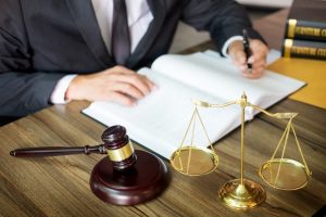 A gavel and sound block rest on a wooden desk, symbolizing justice and law, as a lawyer works in the background.