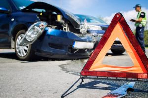 A car accident at an intersection features damaged vehicles and a warning triangle placed on the road to alert approaching traffic.