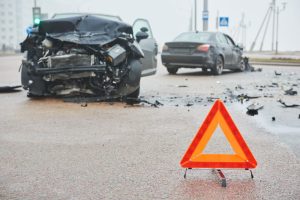 A collision between two vehicles with a road warning triangle sign in focus. 