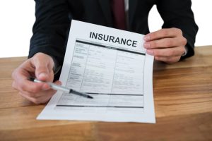 A businessman sits at his desk, holding an insurance contract, with a plain white background highlighting the scene.