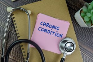 Sticky notes with "Chronic Condition" written on them, placed next to a stethoscope on a wooden table.