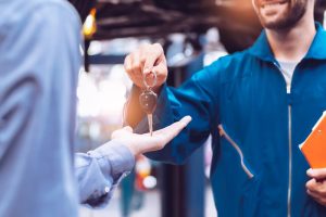 Handsome young car mechanic in uniform is returning car key to a client.