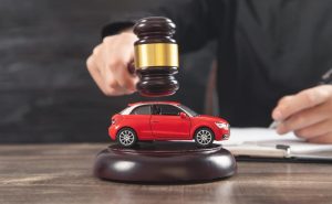 A man strikes a gavel over a car, symbolizing a car auction in progress.