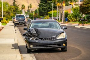 A car accident scene on the road with a smashed front of a passenger car. The car is visibly damaged, with the front bumper crushed and the hood dented.