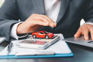 A businesswoman's hand shields a red toy car on her desk, symbolizing her plan to manage transportation finance costs.