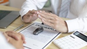 Insurance adjuster inspecting a damaged vehicle, while a sales manager reviews documents and provides guidance on a car insurance application.