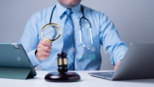 A medical professional uses a magnifying glass to review documents, blending healthcare expertise with legal analysis to ensure compliance and quality standards.