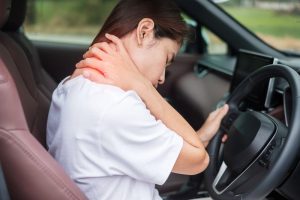 The woman experiencing shoulder and neck pain while driving, reflecting muscle strain and ergonomic challenges.