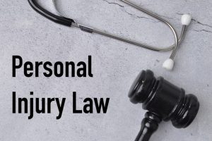 Top view of a stethoscope and a judge’s gavel placed on a grey background with the text "PERSONAL INJURY LAW" written beside them, symbolizing legal and medical aspects.