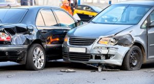 A car crash scene on a street with damaged automobiles, showing crumpled front ends, broken glass, and debris scattered across the road.