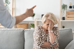 A conceptual image showing an elderly woman sitting in a nursing home while being abused by a caregiver.