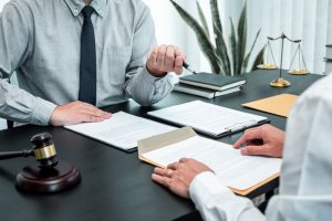 A male lawyer discusses a legal case negotiation with a client in an office, reviewing a contract document. The scene represents law, justice, and the lawsuit process. 