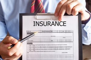 A young man wearing a shirt sits in his office, holding and presenting an insurance policy document.